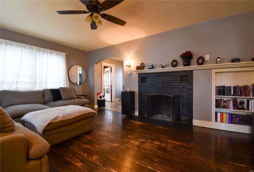 Living room featuring ceiling fan, dark hardwood / wood-style flooring, and a brick fireplace